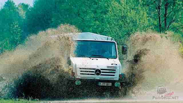 Белый Mercedes-Benz Unimog в брызгах грязи на дороге