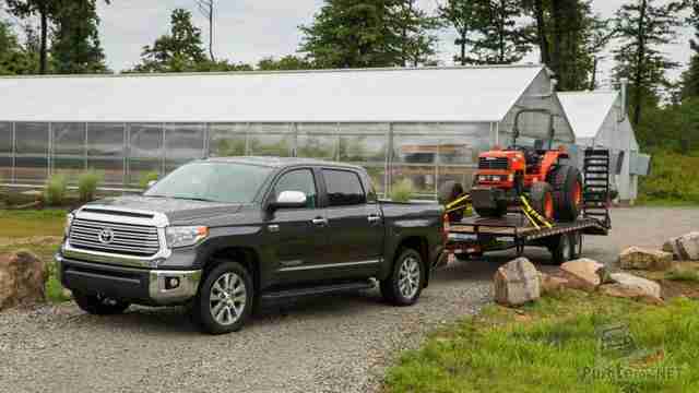 Пикап Toyota Tundra с маленьким трактором на прицепе возле теплиц