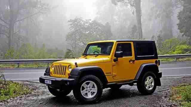 Жёлтый Jeep Wrangler на обочине дороги в лесу