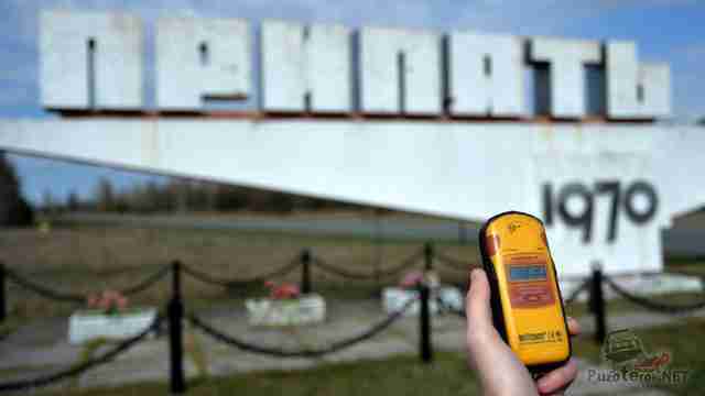 Рука с дозиметром на фоне стелы города Припять Рука с дозиметром на фоне стелы города Припять