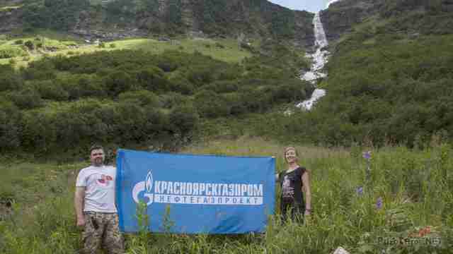 Туристы с корпоративным флагом на фоне водопада Туристы с корпоративным флагом на фоне водопада
